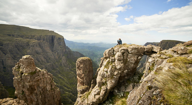 A Female hiker sitting on a rock spire with a with a natural bridge above an epic mountainous valley.