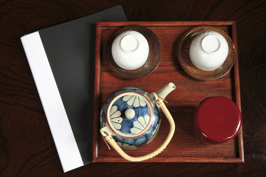 One tea pot, two tea cups, a wooden tray and a document foler in the black background.