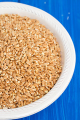 uncooked spelt on white plate on wooden background