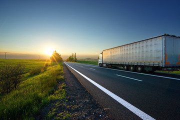 White truck driving on the asphalt road toward the setting sun in the countryside