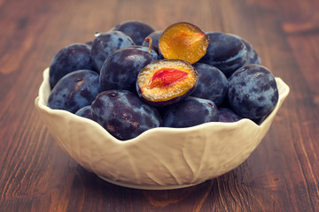 fresh plums in white bowl on wooden background