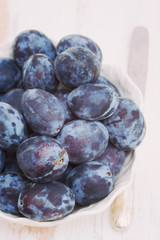 fresh plums in white bowl on wooden background