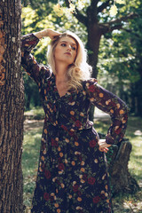 Fashion portrait of happy woman in trendy dress posing in a public garden. Girl with long blonde healthy hair and beautiful smile.