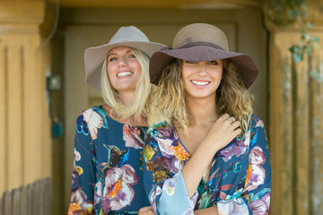 Fashion portrait of two happy woman with blue eyes in flower dress. Fashion hat in a sunny day. Girl with long blonde healthy hair and beautiful smile.