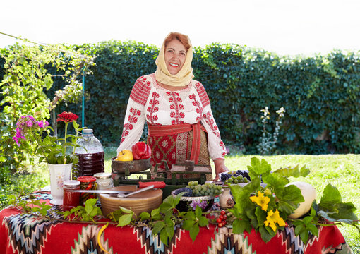 Romanian senior woman dressed in national costume, showing local agricultural products.