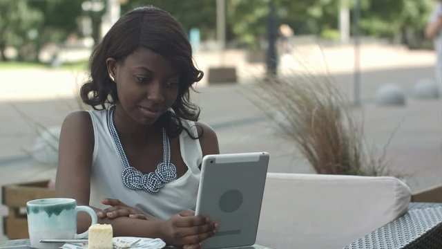 African american woman have video conferance on her tablet sitting in outside cafe