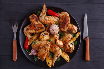 Grilled chicken wings on black plate decorated with garlic, lemon slices and chili peppers. Cooking concept, meat dishes, homemade food