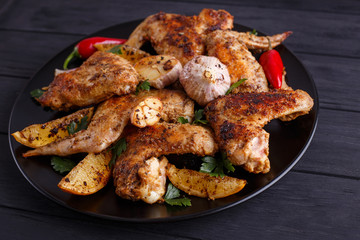 Grilled chicken wings on black plate decorated with garlic and spices. Cooking concept, meat dishes, homemade food