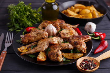 Grilled chicken wings, baked potatoes, herbs and spices on kitchen table, close up. Hot fresh appetizing countryside food. Cooking concept, meat dishes, homemade cuisine