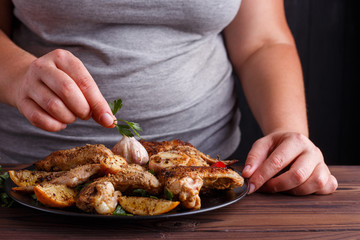 Woman decorating grilled chicken wings with parsley leaves befor