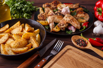 Grilled chicken wings, baked potatoes, herbs and spices on kitchen table. Hot fresh appetizing countryside food. Cooking concept, meat dishes, homemade cuisine