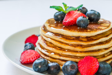American pancakes with blueberries, strawberries, and honey against white background