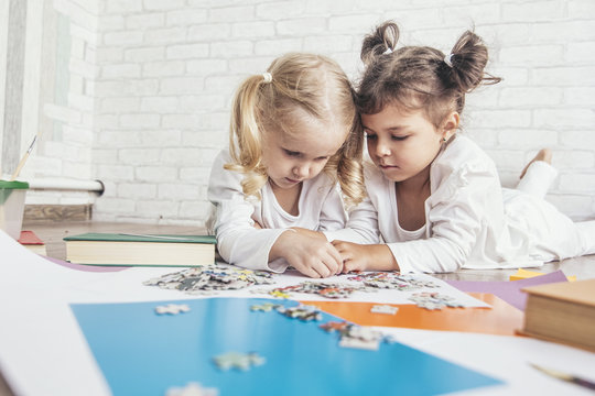Two children, little girls of preschool age put the puzzle together on the floor