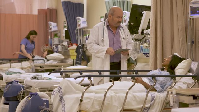 Doctor With Tablet Computer Reviews Test Results With A Patient In Hospital - Wide Shot