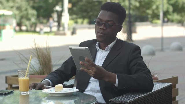 Handsome afro american man is using a tablet, while sitting in outside cafe