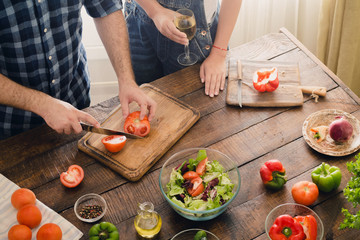 Husband cooking dinner salad while his wife is drinking wine