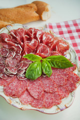 Cold smoked meat plate with pork chops, prosciutto, salami and bread sticks on white wooden background. From top view
