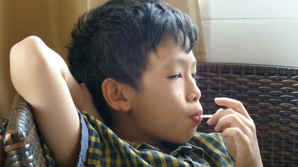 Young asian boy sitting on chair and enjoy eating lollipops 

