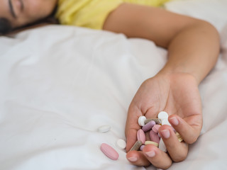Young woman is lying on the bed with a lot of pills. Overdose and suicide concept.