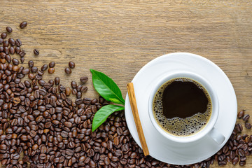 Coffee cup with beans, cinnamon stick and green leaf on wood table