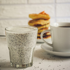 chia seeds with milk in a transparent glass, pancakes and a cup of tea - breakfast on a light background