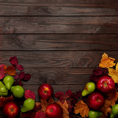 Flat lay frame of autumn crimson and yellow leaves, pears and apples on a dark wooden background.