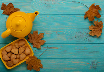 Autumn still life - teapot with a cookie in the form of leaves on a blue wooden background.