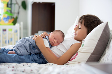 Beautiful boy, hugging with tenderness and care his newborn baby brother at home © Tomsickova