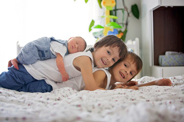 Two children, toddler and his big brother, hugging and kissing their newborn baby brother - obrazy, fototapety, plakaty