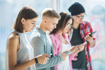 Group of young friends looking at their smart phones without interacting each other indoors. Concepts of lifestyle, technologies and smart phone addiction