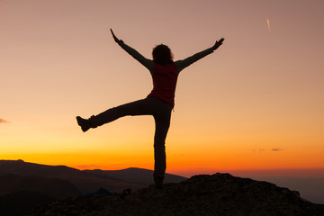 Fototapeta na wymiar Sunset Silhouette of attractive woman staying and looking happy on top of the mountain. Freedom, adventure and leisure vacation concept.