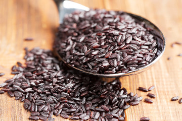 Black rice in a spoon, close-up, wooden background, horizontal, selective focus, high contrast