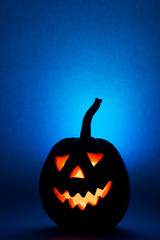 Halloween pumpkin, silhouette of funny face on blue background. Vertical