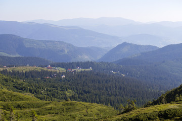 Fototapeta premium Green fir trees and houses of village Dragobrat against background of the Carpathian mountains in the summer. Ukraine