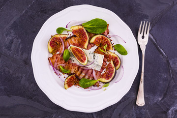 Figs and fried bacon with small lettuce leaves served on a white plate. Italian food. 