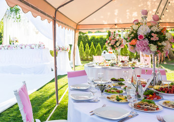 Served round banquet table outdoor in marquee decorated pink flowers and silk