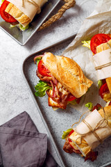 Fresh baguette sandwich bahn-mi styled. Bacon, roasted cheese, tomatoes and lettuce on metallic background. Top view, copy space.