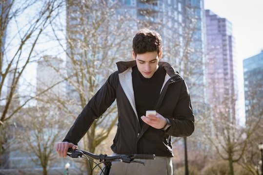 Young man using mobile phone while standing by bicycle