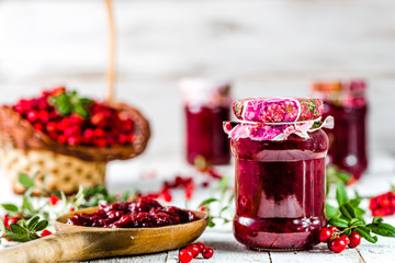 Spoon and jars of jam with cranberry on white wooden background