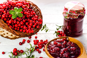 Jars of jam with cranberry on white wooden background