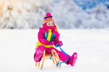 Fototapeta na wymiar Child playing in snow on sleigh in winter park