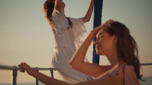 two caucasian young women enjoying breeze sailing on ocean on sunrise while standing in front of yacht in slomo