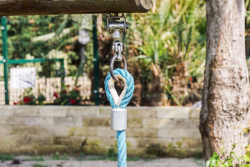 Fototapeta premium End of swinging rope hang on metal construction in a park. Rough rope end in metal circles and safety snap hook