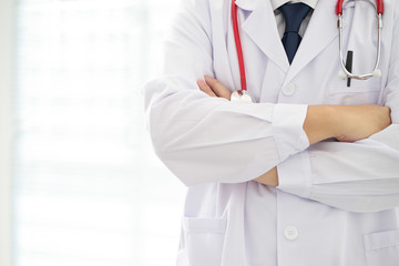 Unknow doctor posing with arms crossed in the office, he is wearing a stethoscope .