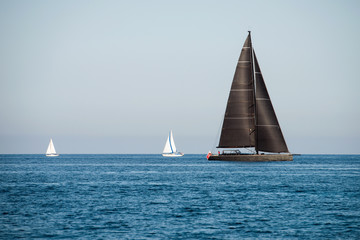 Fototapeta premium Black and two white sailing yachts on the sea with clear blue sky