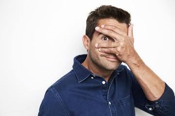 Guy in blue shirt peeking out from hand over eyes