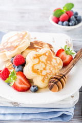 Breakfast with scotch pancakes in flower form, berries and honey on light wooden table. Healthy food concept.