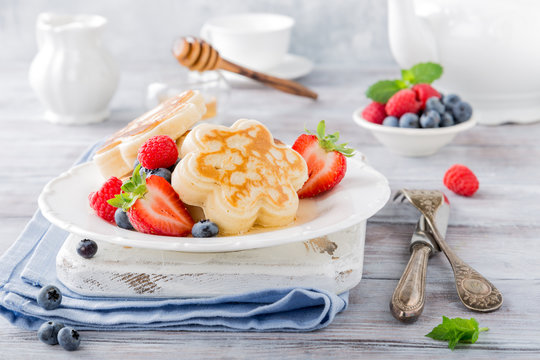 Scotch pancakes in flower form with berries and honey on white wooden background. Healthy breakfast concept.