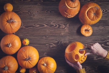 Hands carving jack-o-latern from pumpkin over wooden background, top view, flat lay with copy space for text, toned image