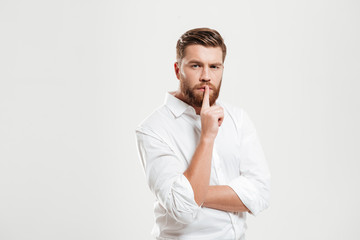 Serious young bearded man showing silence gesture.